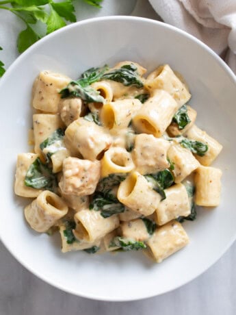 Chicken Spinach Pasta in creamy sauce in a white bowl with Mezza rigatoni pasta.