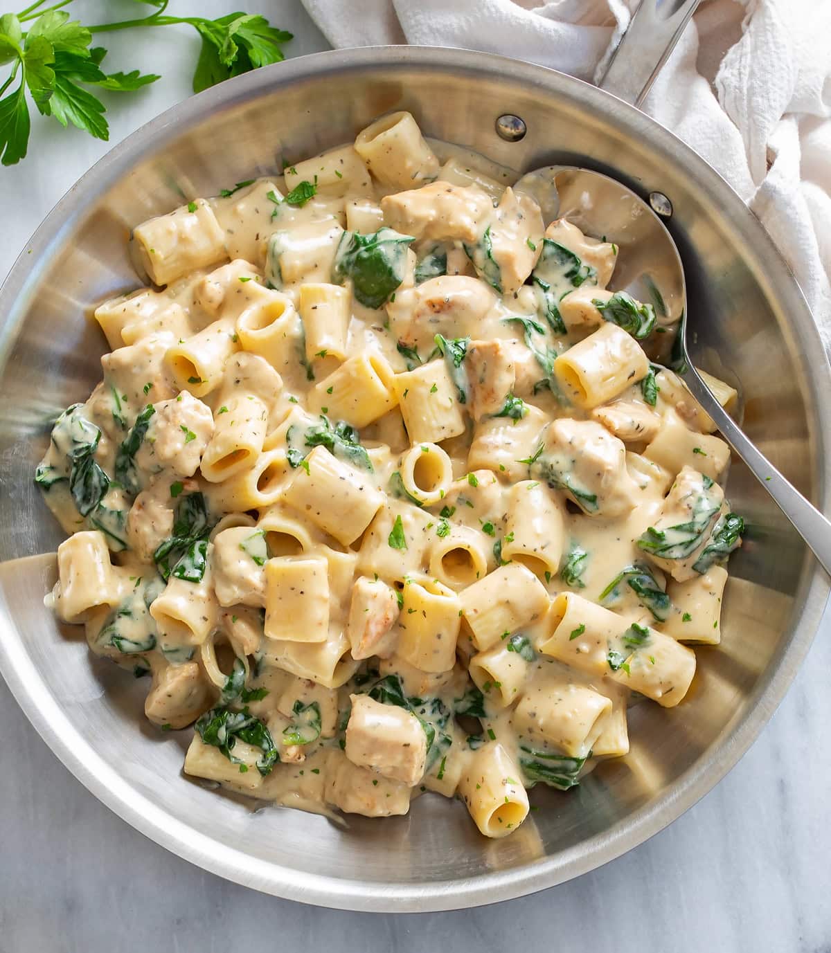 Chicken Spinach Pasta in a stainless steel skillet with a creamy white sauce.