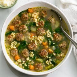 Italian Wedding Soup in a white bowl with a spoon on the side.