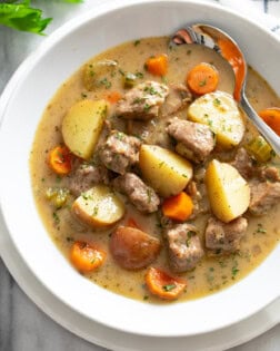 Pork Stew in a white bowl with potatoes, carrots, celery, and onions.