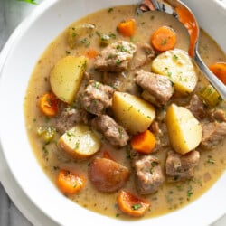 Pork Stew in a white bowl with potatoes, carrots, celery, onions, and bites of pork.