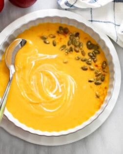 Overhead view of Sweet Potato Soup in a white bowl with swirls of cream and pumpkin seeds on the side.