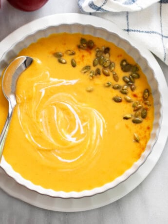 Overhead view of Sweet Potato Soup in a white bowl with swirls of cream and pumpkin seeds on the side.