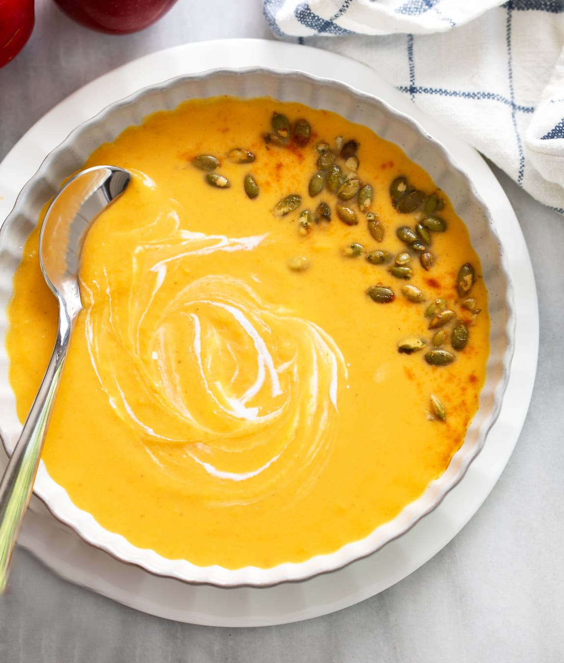 Overhead view of Sweet Potato Soup in a white bowl with swirls of cream and pumpkin seeds on the side.