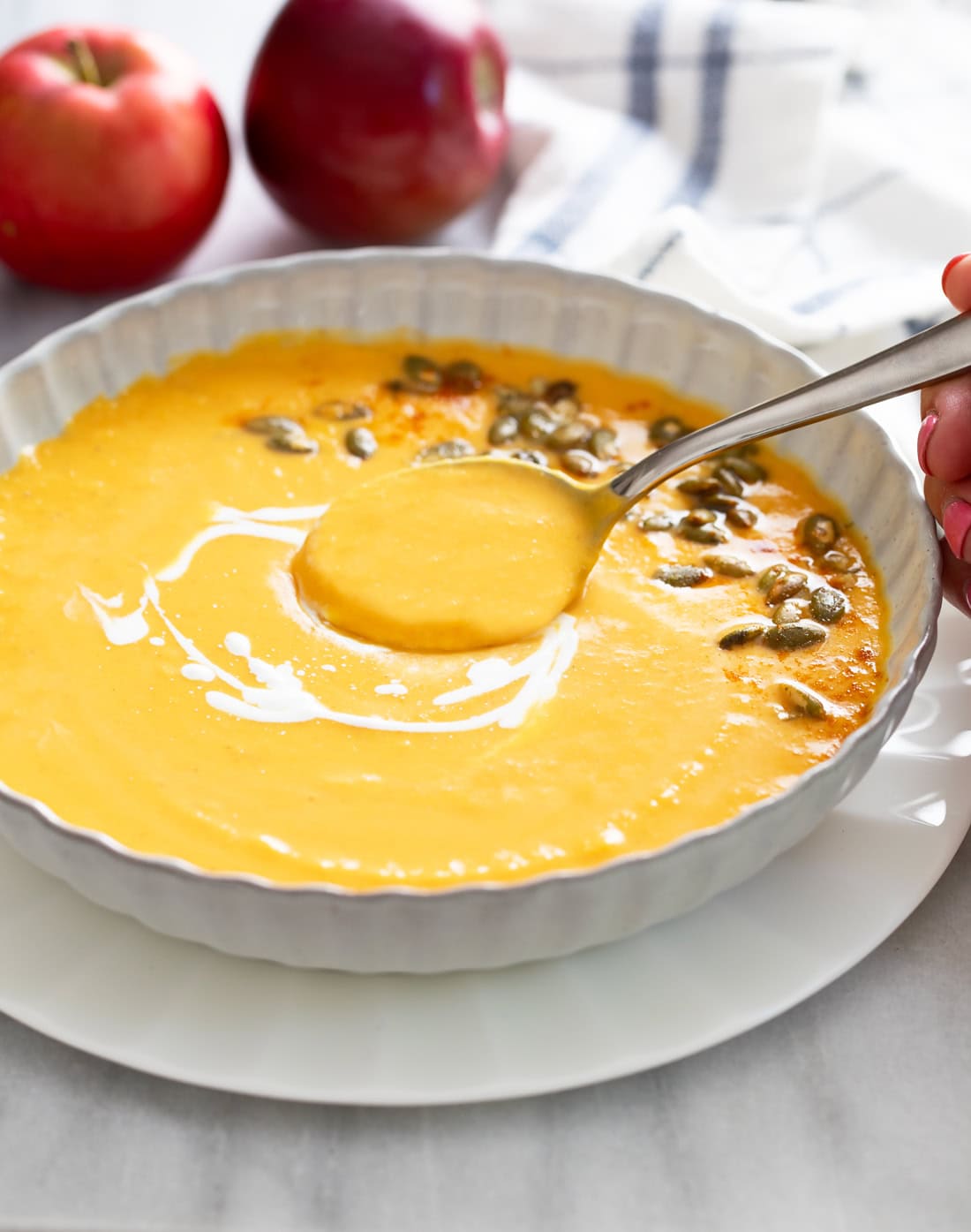 A spoon scooping up Sweet Potato Soup from a white bowl with swirls of cream on top.