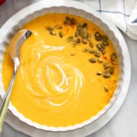 Sweet Potato Soup in a white bowl with pumpkin seeds, paprika, and a swirl of cream as garnishes.