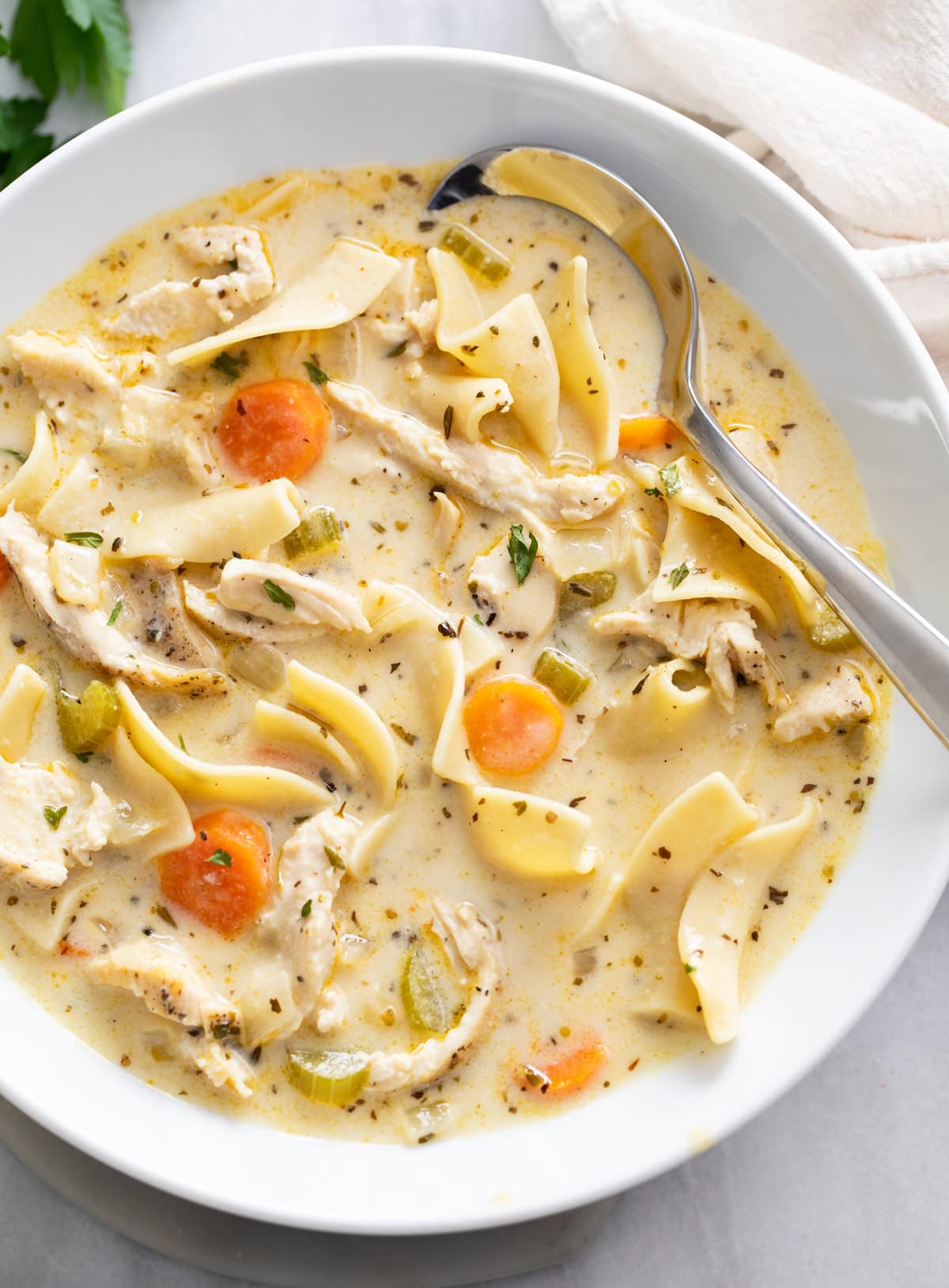 Creamy Chicken Noodle Soup in a white bowl with a spoon on the side.