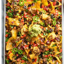 Nachos on a sheet pan loaded with toppings like ground beef, refried beans, and cheese.