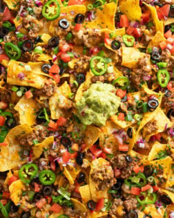 Nachos on a sheet pan loaded with toppings like ground beef, refried beans, and cheese.