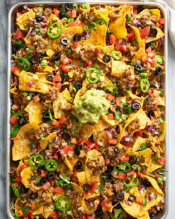 A tray of Loaded Nachos with beef, refried beans, cheese, olives, jalapenos, and more.