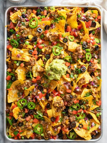 A tray of Loaded Nachos with beef, refried beans, cheese, olives, jalapenos, and more.