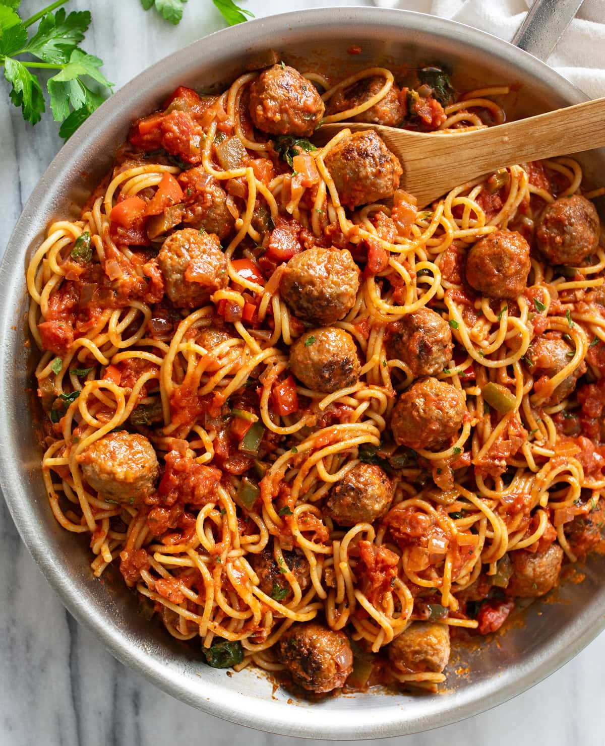 A skillet filled with Sausage Spaghetti with a wooden spoon on the top.