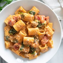 Creamy Tomato Spinach Pasta in a white bowl with tomatoes, sausage, and spinach.