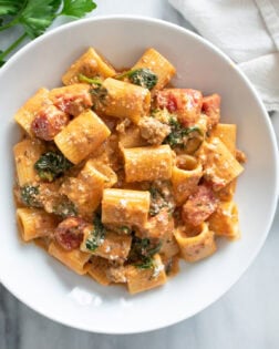 Tomato Spinach Pasta in a white bowl with parmesan cheese sprinkled on top.