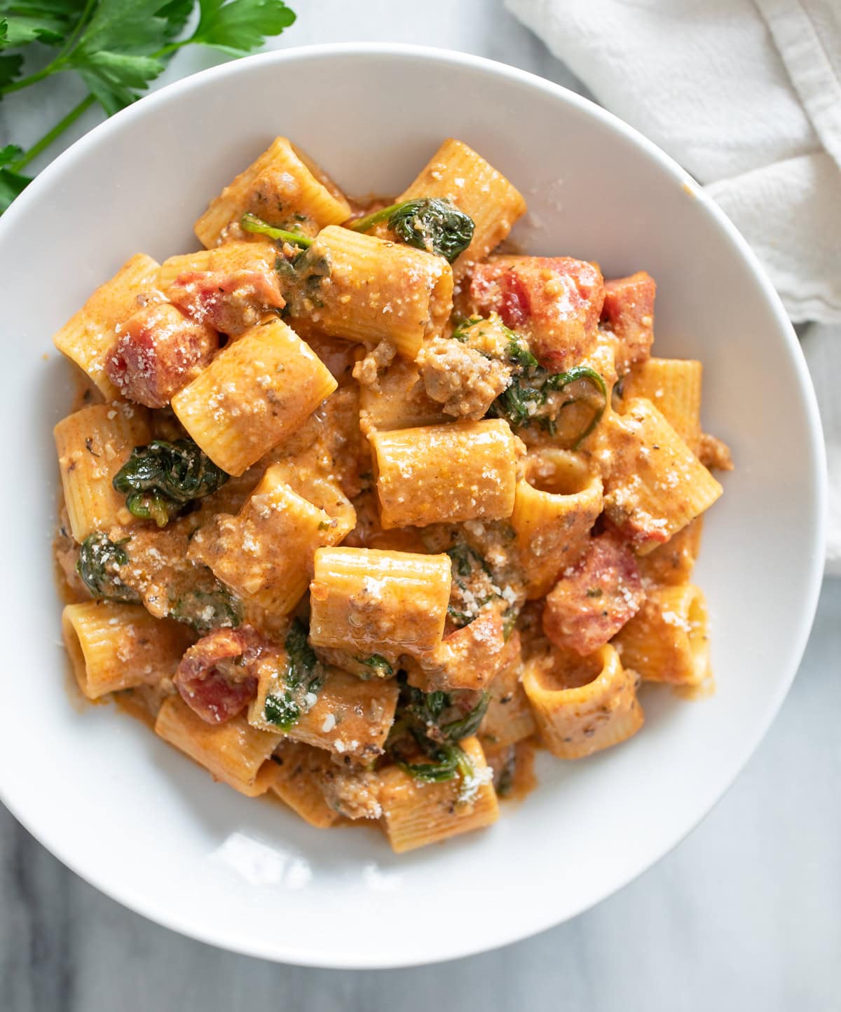 Tomato Spinach Pasta in a white bowl with parmesan cheese sprinkled on top.