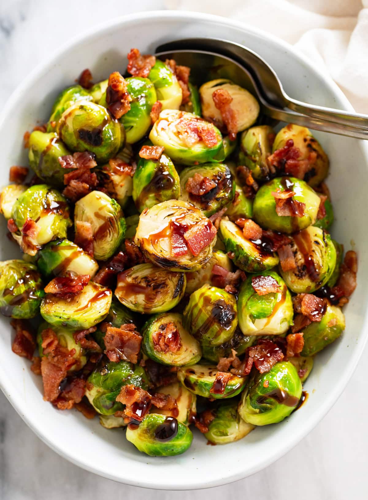 Overhead view of Bacon Brussels Sprouts in a white bowl with balsamic glaze on top.