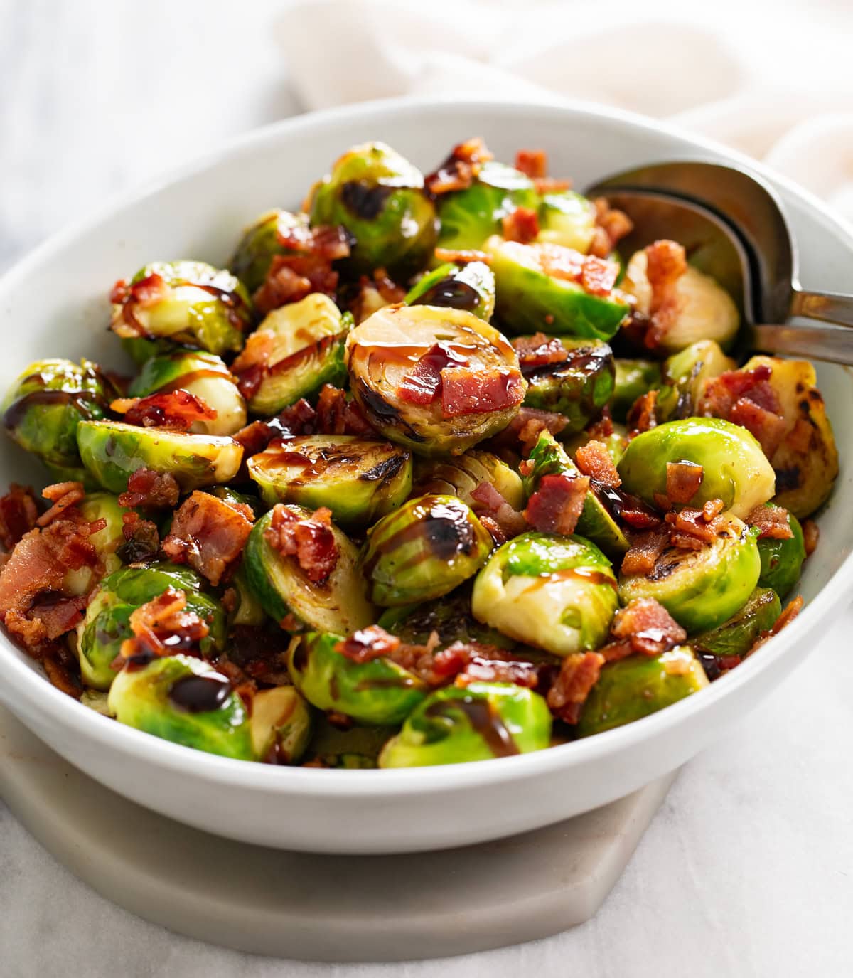 Side view of Bacon Brussels Sprouts drizzled with balsamic glaze in a white bowl.