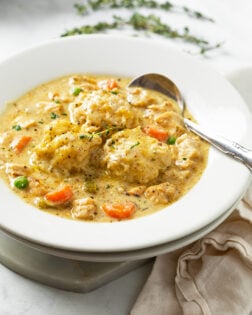 Chicken and Dumplings in a white bowl with fresh thyme in the background.