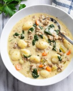 A white bowl of Sausage Gnocchi Soup with a spoon on the side.