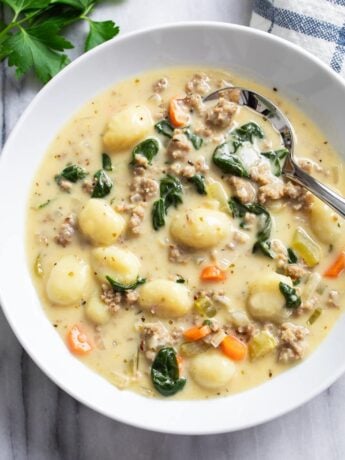 A white bowl of Sausage Gnocchi Soup with a spoon on the side.