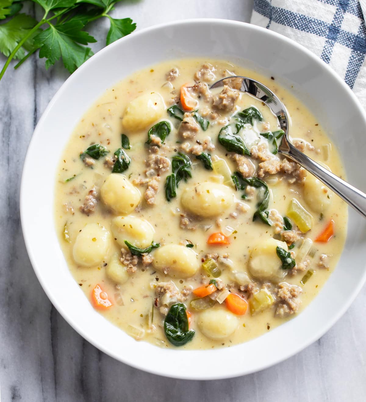 A white bowl of Sausage Gnocchi Soup with a spoon on the side.