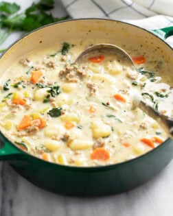 A green Dutch oven filled with Sausage Gnocchi Soup with a ladle on the side.