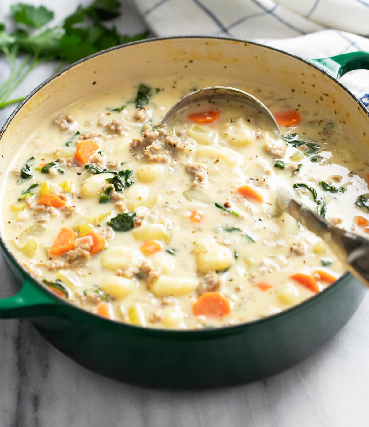 A green Dutch oven filled with Sausage Gnocchi Soup with a ladle on the side.