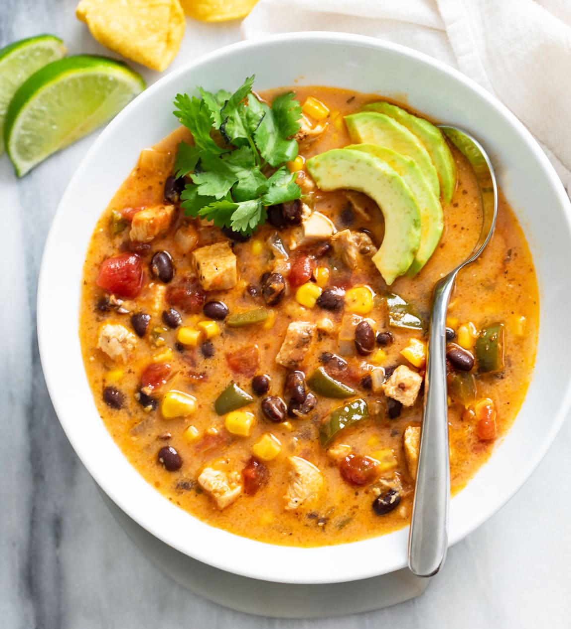 Chicken Poblano Soup in a white bowl with cilantro and avocado on top and a spoon on the side.