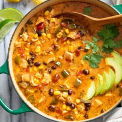 Chicken Poblano Soup in a green Dutch Oven with a wooden spoon on the side and avocado slices on top.