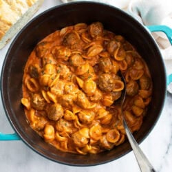 A pot of Meatball Pasta in a creamy tomato sauce with mini meatballs and a spoon on the side.