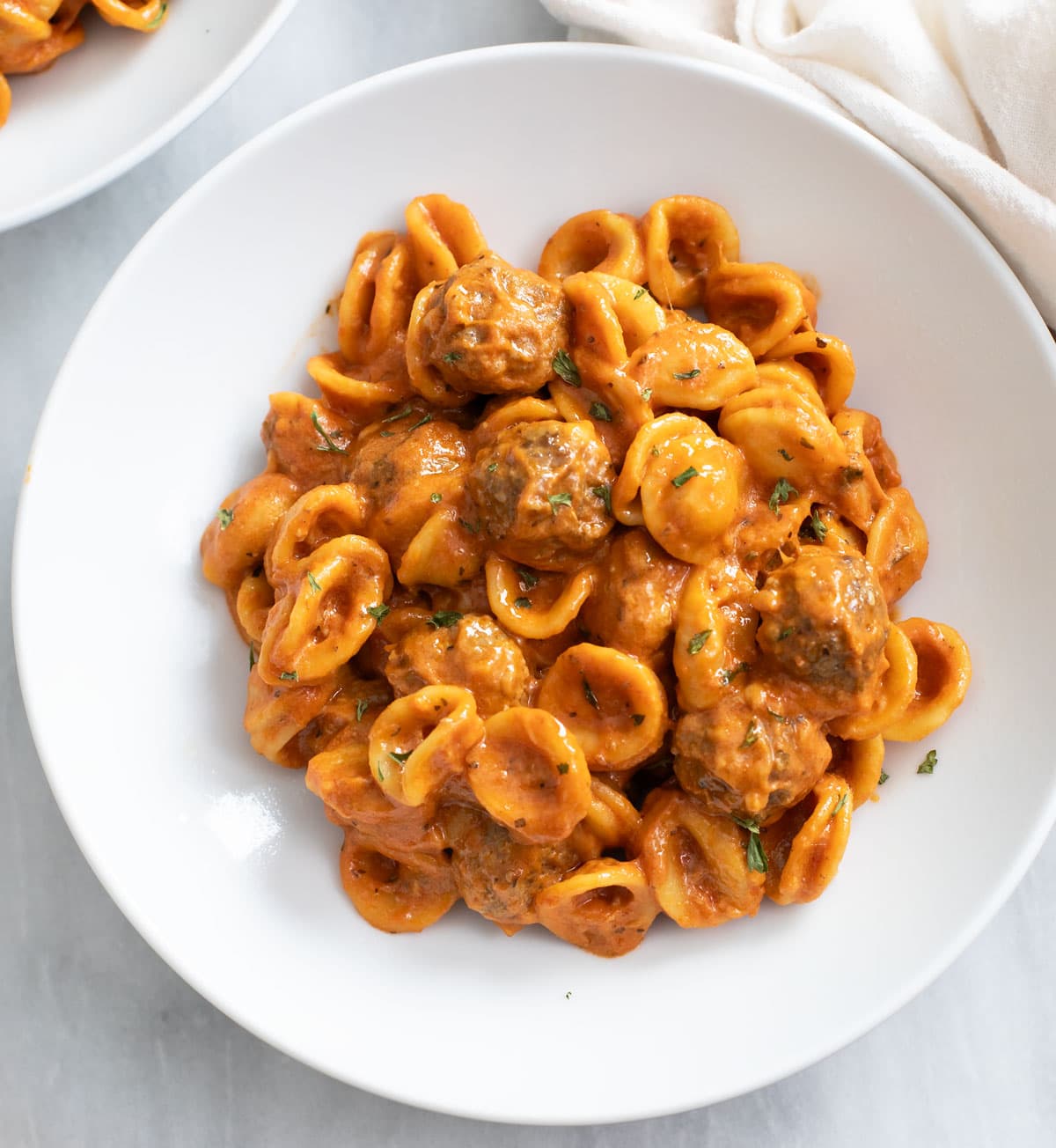 Meatball Pasta in a creamy tomato sauce on a white plate with mini meatballs.