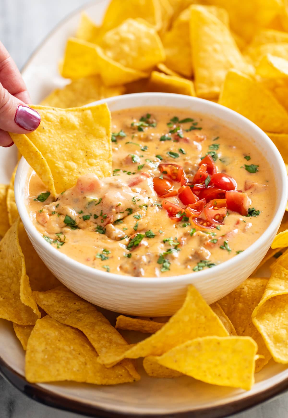 A hand dipping a tortilla chip into a white bowl of Rotel Dip.