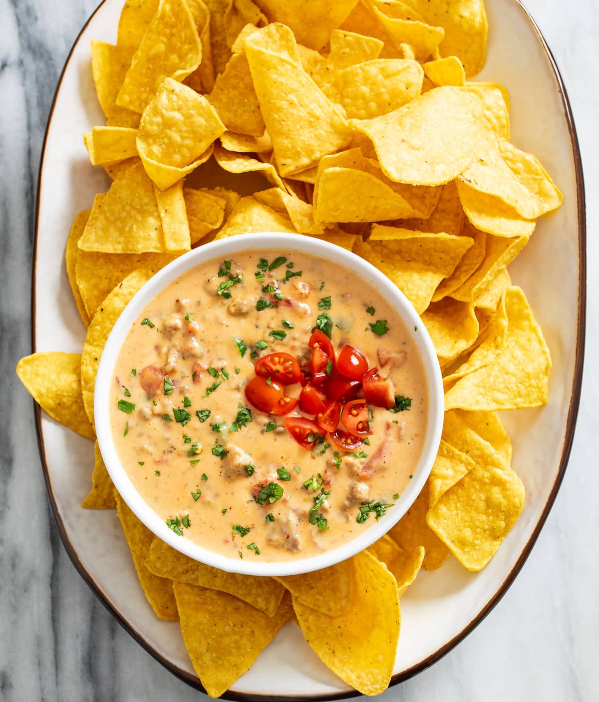 A platter of tortilla chips with a bowl of Rotel dip with diced tomatoes and cilantro on top.