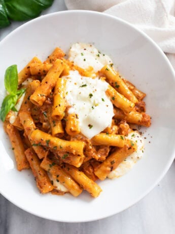 Burrata Pasta on a white plate with tomato sauce and dollops of burrata on top.