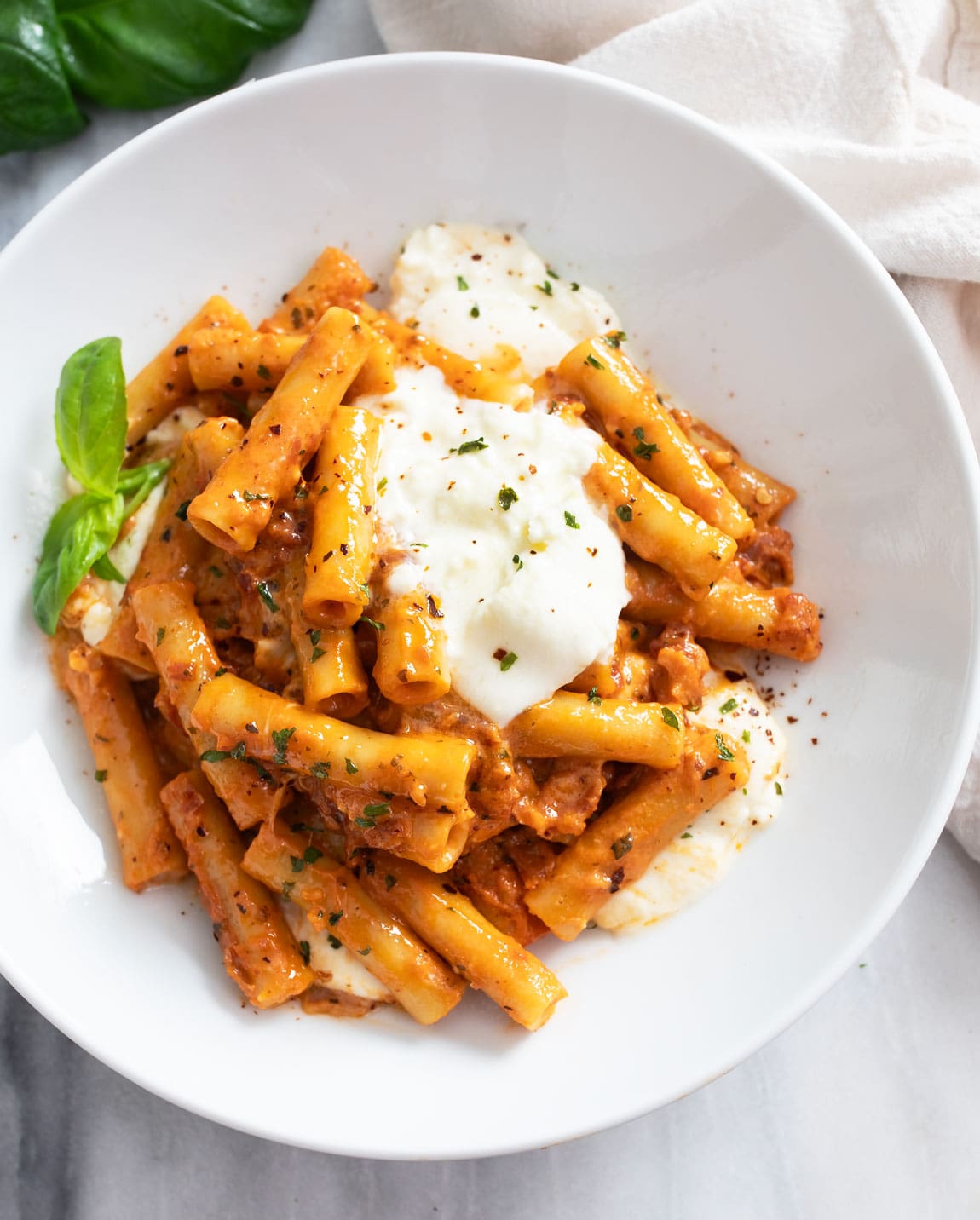 Burrata Pasta on a white plate with tomato sauce and dollops of burrata on top.