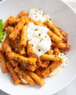 Burrata Pasta on a white plate with fresh basil on the side and creamy burrata cheese on top.