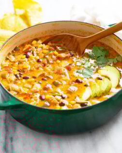 Chicken Poblano Soup in a green Dutch oven with sliced avocado on top and a spoon on the back.