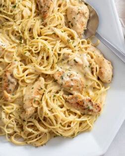 Garlic Parmesan Chicken Pasta on a white tray with a spoon on the side and parsley on top.