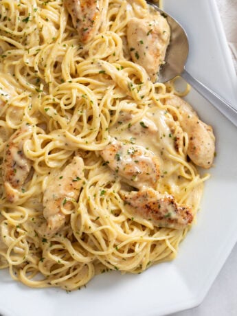 Garlic Parmesan Chicken Pasta on a white tray with a spoon on the side and parsley on top.