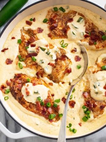 A skillet filled with Jalapeno Popper Chicken in a cream sauce with bacon and green onions.