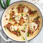 Jalapeno Popper Chicken in a skillet with bacon and green onions on top and a spoon in the middle.