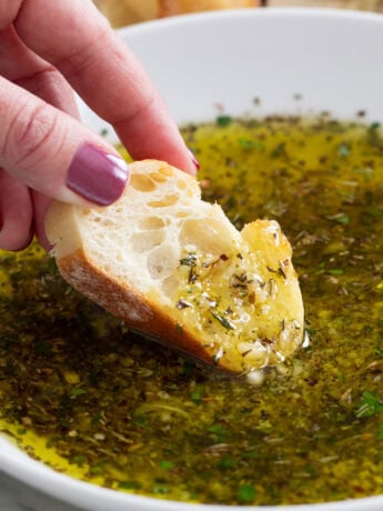 A slice of crusty bread being dipped into Olive Oil Bread Dip.