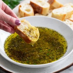 A slice of crusty bread being dipped into a bowl of Olive Oil Bread Dip.