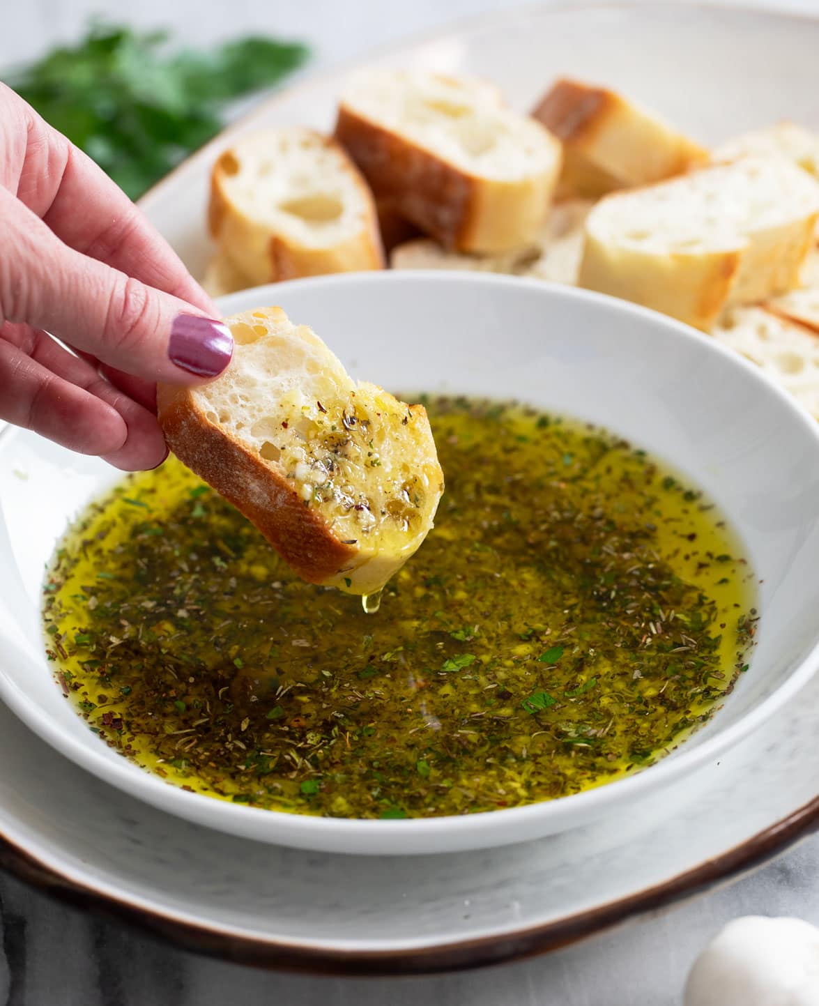 Olive Oil Bread Dip in a white bowl with a hand dipping a slice of crusty bread into it.