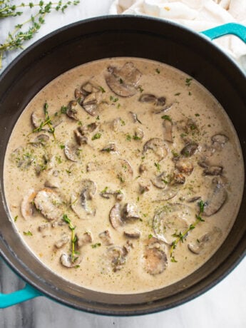 A soup pot filled with Cream of Mushroom Soup with fresh thyme on top.