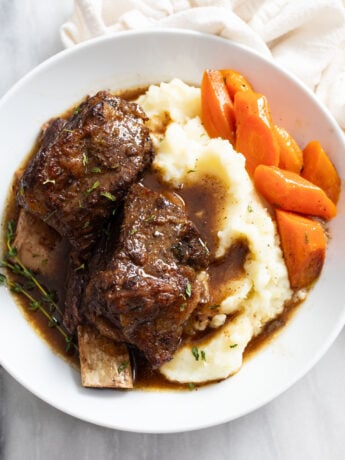 Slow Cooker Short Ribs on a white plate with mashed potatoes and carrots.