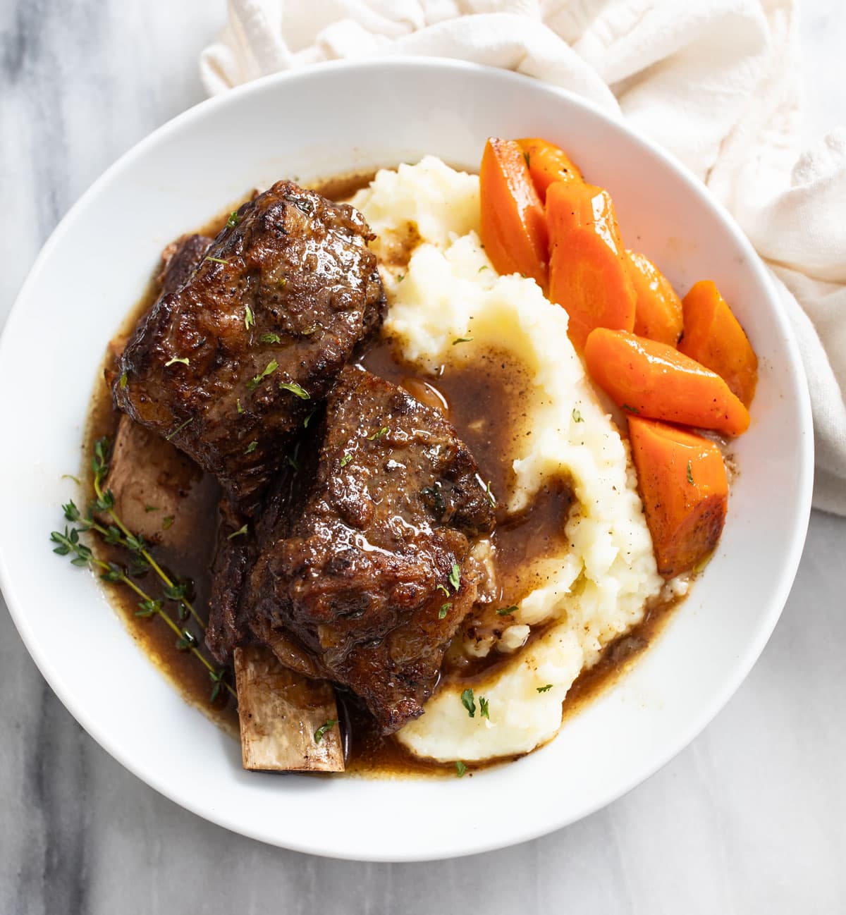 Slow Cooker Short Ribs on a white plate with mashed potatoes and carrots.