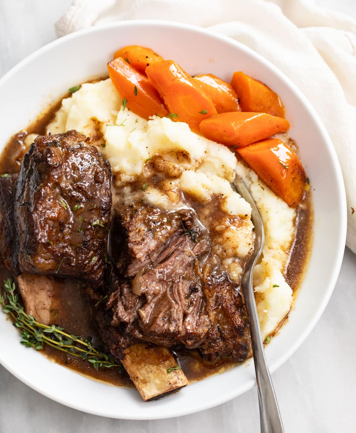 Slow Cooker Short Ribs on a pile of mashed potatoes with gravy and carrots.