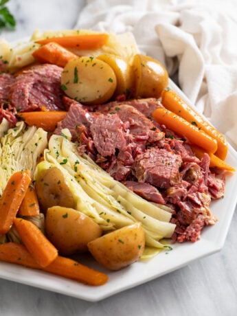 Corned Beef and Cabbage on a white platter with carrots and potatoes.