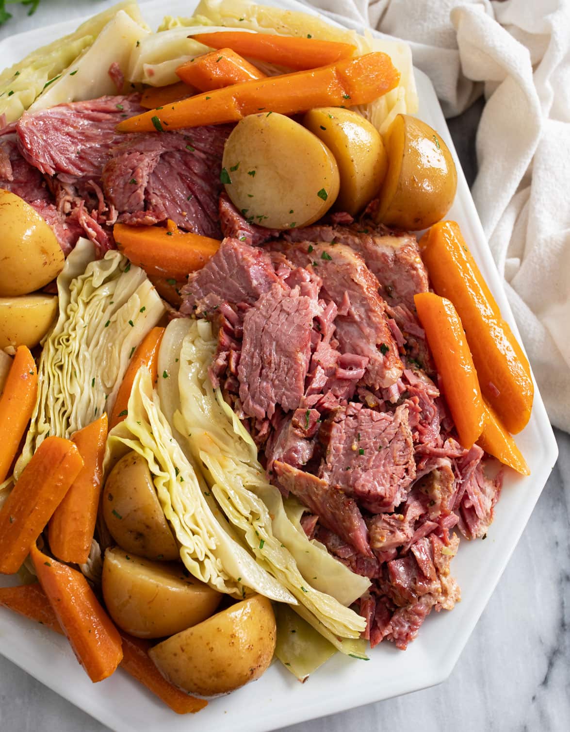 A white platter with Corned Beef and Cabbage along with carrots and potatoes.